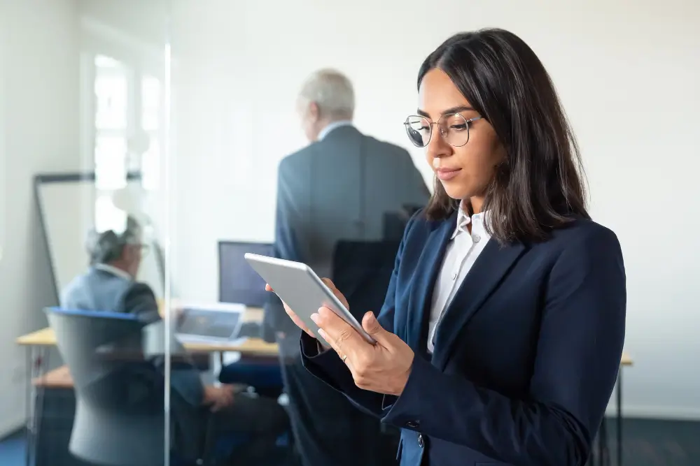 Businesswoman in formal suit using a tablet in a glass-walled office.