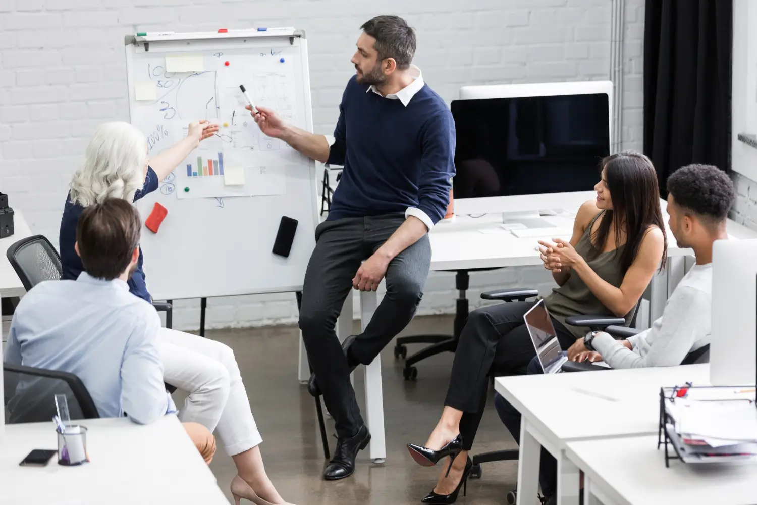 Group of colleagues in office meeting analyzing charts on a whiteboard.