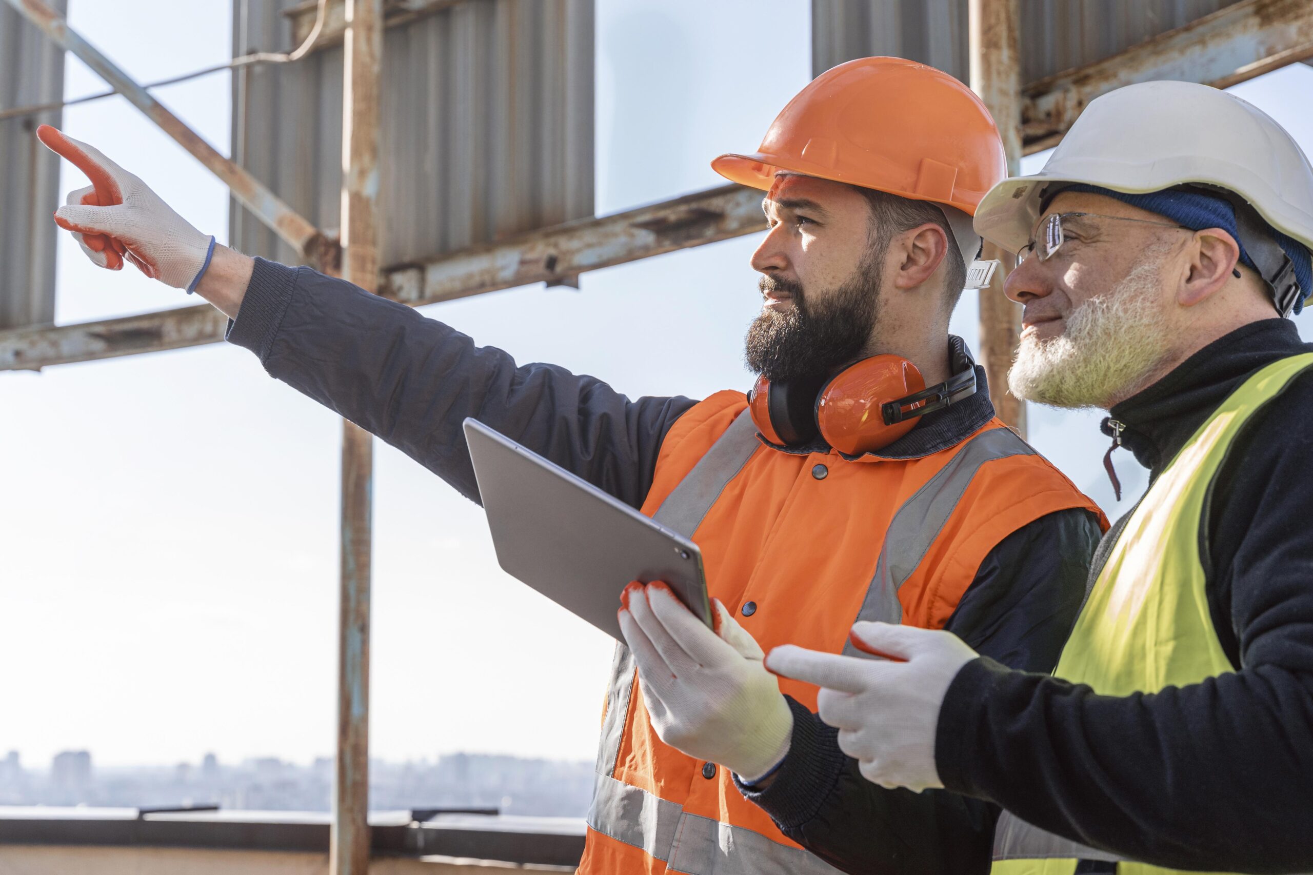 two construction workers wearing helmets using tablet at building site
